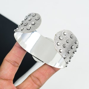 May include: A silver cuff bracelet with a textured surface and small raised dots. The bracelet is open and has a curved shape.