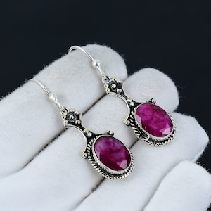 May include: A pair of silver earrings with a pink gemstone in an oval shape. The earrings have a detailed design with gold accents.
