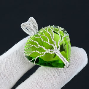 May include: A silver wire tree of life pendant with a green heart-shaped glass stone.