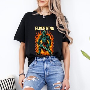 May include: Black t-shirt with a graphic of a knight in armor holding a sword, standing in flames. The text "ELDEN RING" is above the graphic.
