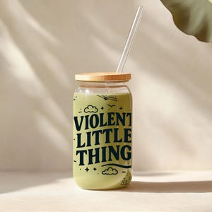 Puede incluir: Un tarro de vidrio con tapa de madera y una pajita. El tarro est&aacute; lleno de un l&iacute;quido verde y tiene el texto "VIOLENT LITTLE THING" impreso en &eacute;l.