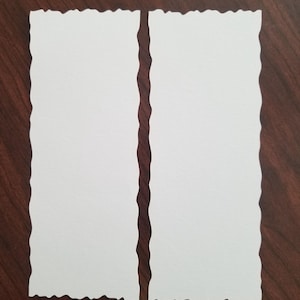 May include: Two rectangular white paper sheets with torn edges are displayed on a dark brown wooden surface. The torn edges give the paper a unique, textured appearance. The paper is blank, suggesting it is intended for writing or drawing.
