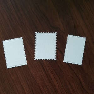 May include: Three white blank paper labels with scalloped edges. The labels are on a brown wooden surface.