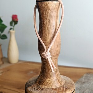 May include: A wooden mallet with a dark brown finish and a black band around the top. A light brown leather loop is attached to the top of the mallet.