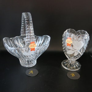 May include: Two clear glass bowls, one with a handle and a swirl design, the other heart-shaped with an etched floral design. Both bowls have a label that reads "Anna-Home Bohemia".
