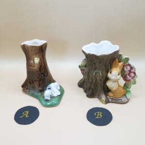 May include: Two ceramic tree stump vases, one with a white puppy and the other with a brown rabbit. The vases are brown with green leaves and flowers.