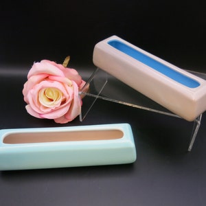 May include: Three rectangular ceramic vases in the image. One is light blue with a brown interior, another is beige with a blue interior, and the third is light blue with a brown interior. A pink rose is in the background.