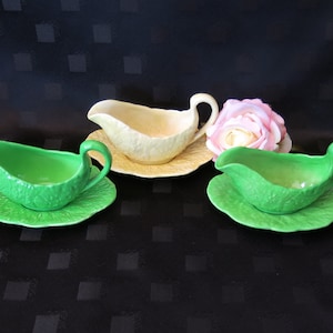 Puede incluir: Tres salseras de cerámica, dos verdes y una amarilla, con platos a juego con forma de hojas de col.