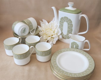 May include: A set of green and white teacups, saucers, and a teapot with a matching creamer. The teacups and saucers have a delicate floral pattern with gold accents. The teapot has a square body and a lid with a finial.