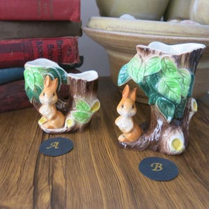 May include: Two ceramic squirrel planters, one larger than the other, shaped like tree trunks with green leaves and a squirrel on each. The smaller planter is labelled "A" and the larger planter is labelled "B".