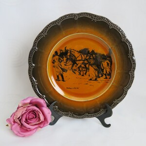 May include: A decorative plate with a scalloped edge and a brown and orange color scheme. The plate features a black illustration of people and horses. The text "Working in the field" is visible on the plate.