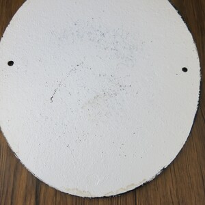 May include: White round metal sign with two small holes near the edge. The sign has a slightly textured surface and appears to be blank.