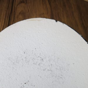 May include: White round ceramic plate with a black rim. The plate has a textured surface and some black specks.