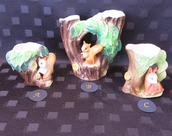 May include: Three ceramic squirrel planters, each featuring a different squirrel design. The planters are shaped like tree trunks with green leaves and brown bark. The squirrels are brown and white with bushy tails.