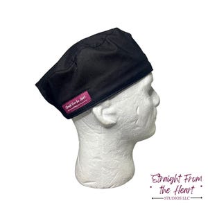 Puede incluir: Un gorro quirúrgico negro con una etiqueta rectangular magenta que dice "Straight From the Heart - STUDIOS LLC". El gorro se muestra en una cabeza de maniquí blanca. El gorro está hecho de una tela suave y duradera.