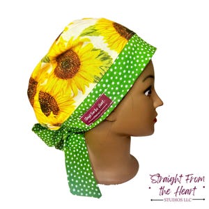 May include: A scrub cap featuring a sunflower print with yellow petals and brown centers. The cap has a green polka dot trim and a matching tie. The label reads "Straight From the Heart".