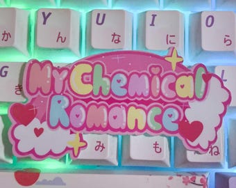 May include: A pink and white sticker with the text "My Chemical Romance" in rainbow letters. The sticker is on a white keyboard with Japanese characters on the keys.