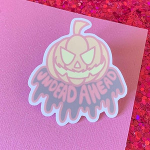 May include: A pink and black sticker with a cartoon pumpkin and the text "UNDEAD AHEAD" dripping from the bottom.