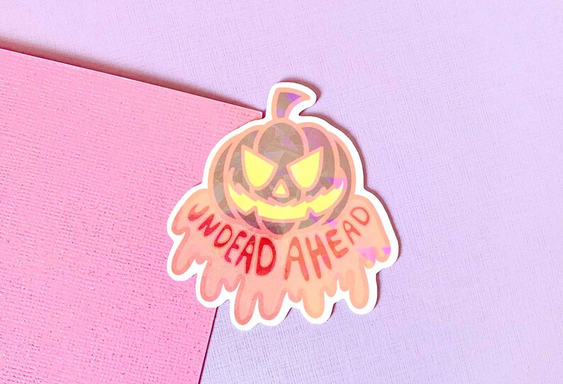 May include: A holographic sticker with a dripping orange pumpkin and the text "UNDEAD AHEAD" in red.