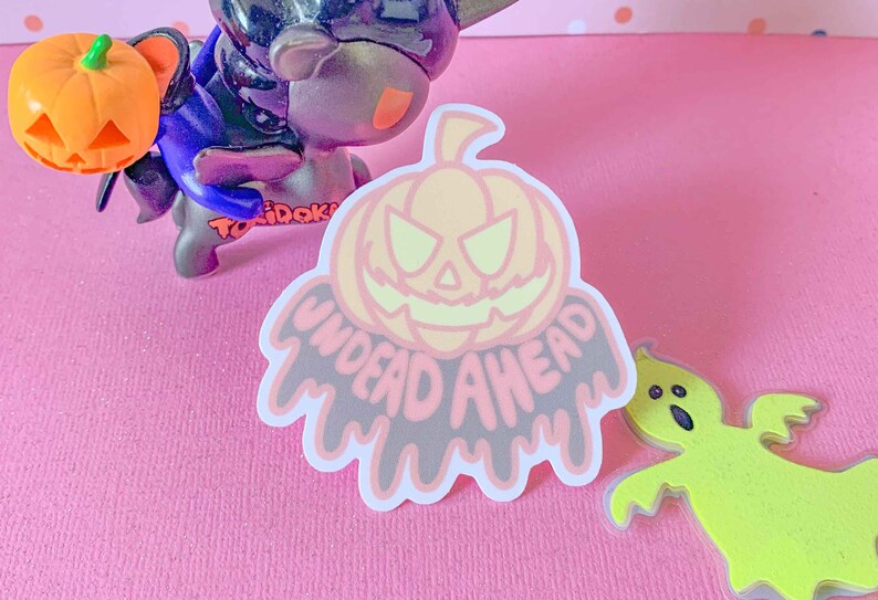 May include: A pink and white sticker with a cartoon pumpkin face and the text "UNDEAD AHEAD" in dripping black letters.