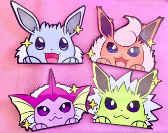 May include: Four colorful cartoon character pins. The pins feature a light blue, orange, pink, and green creature with large eyes and star accents. The characters have a happy expression and are set against a pink background.