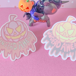 May include: Two Halloween-themed stickers with a dripping pumpkin design. The stickers are pink and gray with the text "Undead Ahead" in a dripping font.