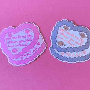 May include: Two heart-shaped cake stickers with pink and blue frosting. The stickers feature the text "You made me the villain you can't live without" and "miu".