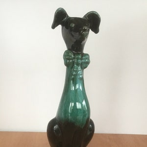 Puede incluir: Una figurita de perro de cerámica negra y verde con una pajarita verde. El perro está sentado con la cabeza inclinada hacia arriba.