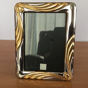 May include: A silver and gold picture frame with a decorative, ornate design. The frame has a rectangular shape and a smooth, polished finish.