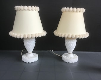 May include: Two white milk glass table lamps with cream colored pom-pom trimmed lampshades.
