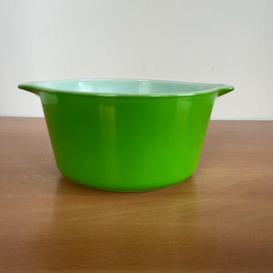 May include: A bright lime green mixing bowl with a smooth, glossy finish. The bowl features a wide, circular opening, a deep basin, and two integrated handles on opposite sides. The interior of the bowl is a pale, light mint green colour.