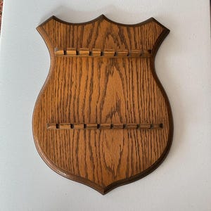Peut inclure: Un support mural en bois en forme de bouclier avec des fentes pour l'affichage d'objets. Le bouclier est en bois de chêne avec une teinte brun foncé.