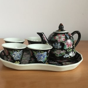 Könnte beinhalten: Ein schwarzes und weißes Porzellan-Tee-Set mit Blumendesigns. Das Set enthält eine Teekanne, vier Tassen und ein Tablett.