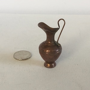 May include: A small copper jug with a handle. The jug is about the size of a UK 20 pence coin.