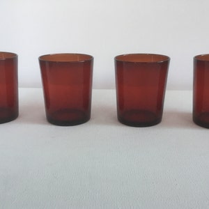 May include: Four dark red glass tumblers on a white surface.