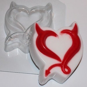 May include: A clear plastic mold for making a heart-shaped soap with devil horns and a red tail. The mold is shown with a finished soap inside.