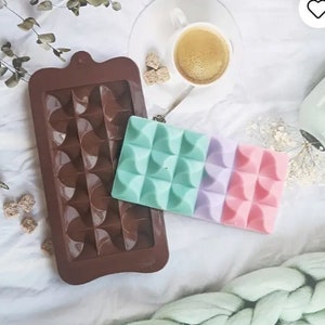 May include: A brown silicone chocolate mold with a geometric pattern. A three-section chocolate bar with a mint green, lavender, and pink geometric pattern is sitting on top of the mold.