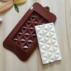 May include: A brown silicone chocolate mold with a diamond pattern. A white chocolate bar with a diamond pattern is next to the mold.