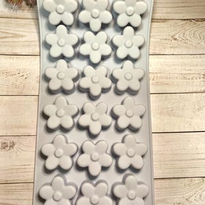 May include: A light gray silicone mold with 15 flower-shaped cavities. Each flower has five petals and a circular center. The mold is designed for creating decorative items, such as soaps or candies.