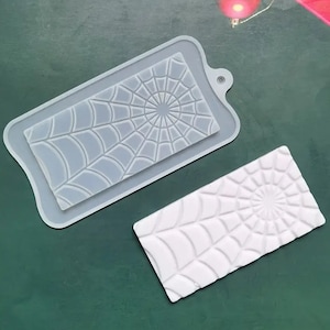 May include: Two silicone molds for making chocolate or candy. The molds are shaped like a spider web. One mold is white and the other is gray.