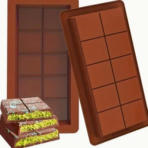 May include: Two brown silicone chocolate molds with nine squares each. The molds are open and show the inside of the squares. A stack of three chocolate bars with green and white frosting is in front of the molds.