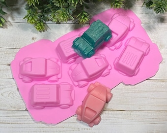 May include: Pink silicone mold with six car-shaped cavities. The mold is designed to create small, detailed car-shaped soaps, candles, or other crafts. One cavity is filled with a teal-colored car.