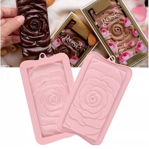 May include: Two pink silicone molds for making chocolate bars. Each mold features a raised design of a rose.