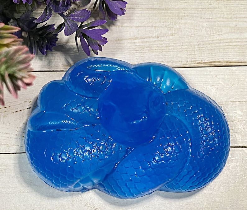 May include: A blue soap bar shaped like a coiled snake. The soap has a textured surface and is made in the shape of a snake curled up.