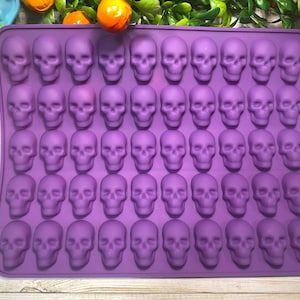 May include: A purple silicone mold with 40 skull-shaped cavities. The mold is rectangular and designed for making candies, chocolates, or ice cubes. The skulls are detailed and evenly spaced.