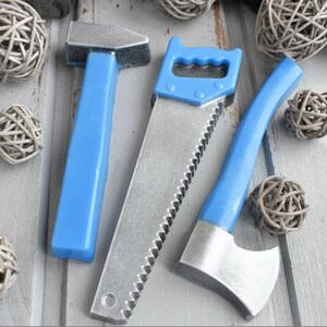 May include: Three toy tools made of plastic and metal. A blue hammer, a blue saw with a silver blade, and a blue axe with a silver blade.