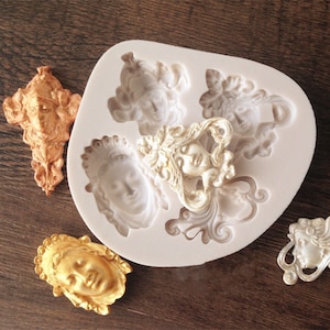 May include: A silicone mold for making decorative cake toppers. The mold features five different designs of women's faces with ornate details. The mold is white and is shown with gold-colored cake toppers.