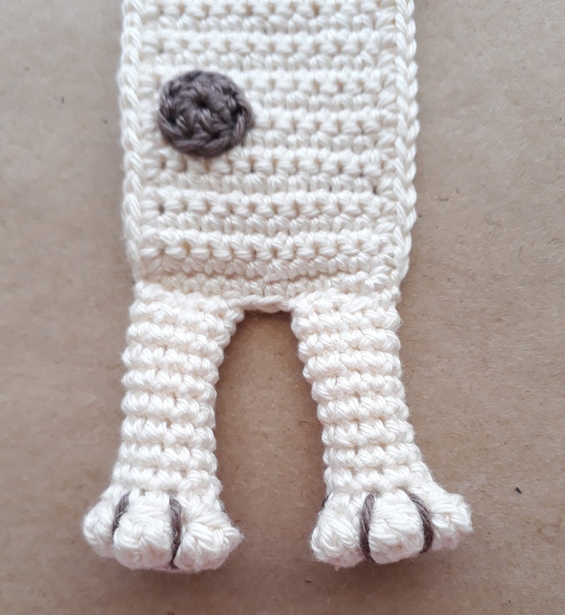Puede incluir: Marcap&aacute;ginas de crochet blanco con detalles marrones. El marcap&aacute;ginas tiene forma de perro con dos patas y una nariz marr&oacute;n.