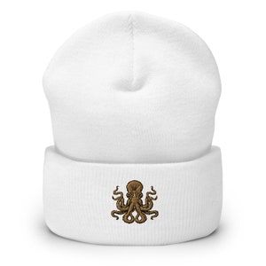 Könnte beinhalten: Weiße Strickmütze mit einem braunen gestickten Kraken-Design.