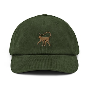 Può includere: Un berretto da baseball in velluto a coste verde con una silhouette di scimmia ricamata in marrone.